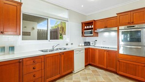 A kitchen with wooden cabinets, a dishwasher, a microwave, a toaster, and a double oven. - Welcome to The Lookout, a beautiful 4 bedroom house with stunning ocean views. (Coffs Harbour)
