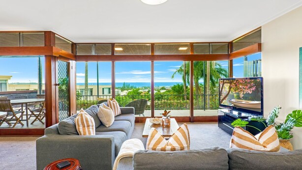 A spacious living room with a large window overlooking a scenic view, a comfortable sofa, a coffee table, and a television. - Welcome to The Lookout, a beautiful 4 bedroom house with stunning ocean views. (Coffs Harbour)