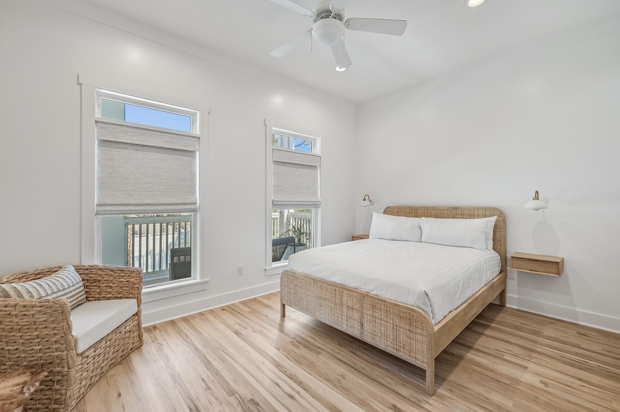 A bedroom with a large bed, a wicker chair, and a ceiling fan.