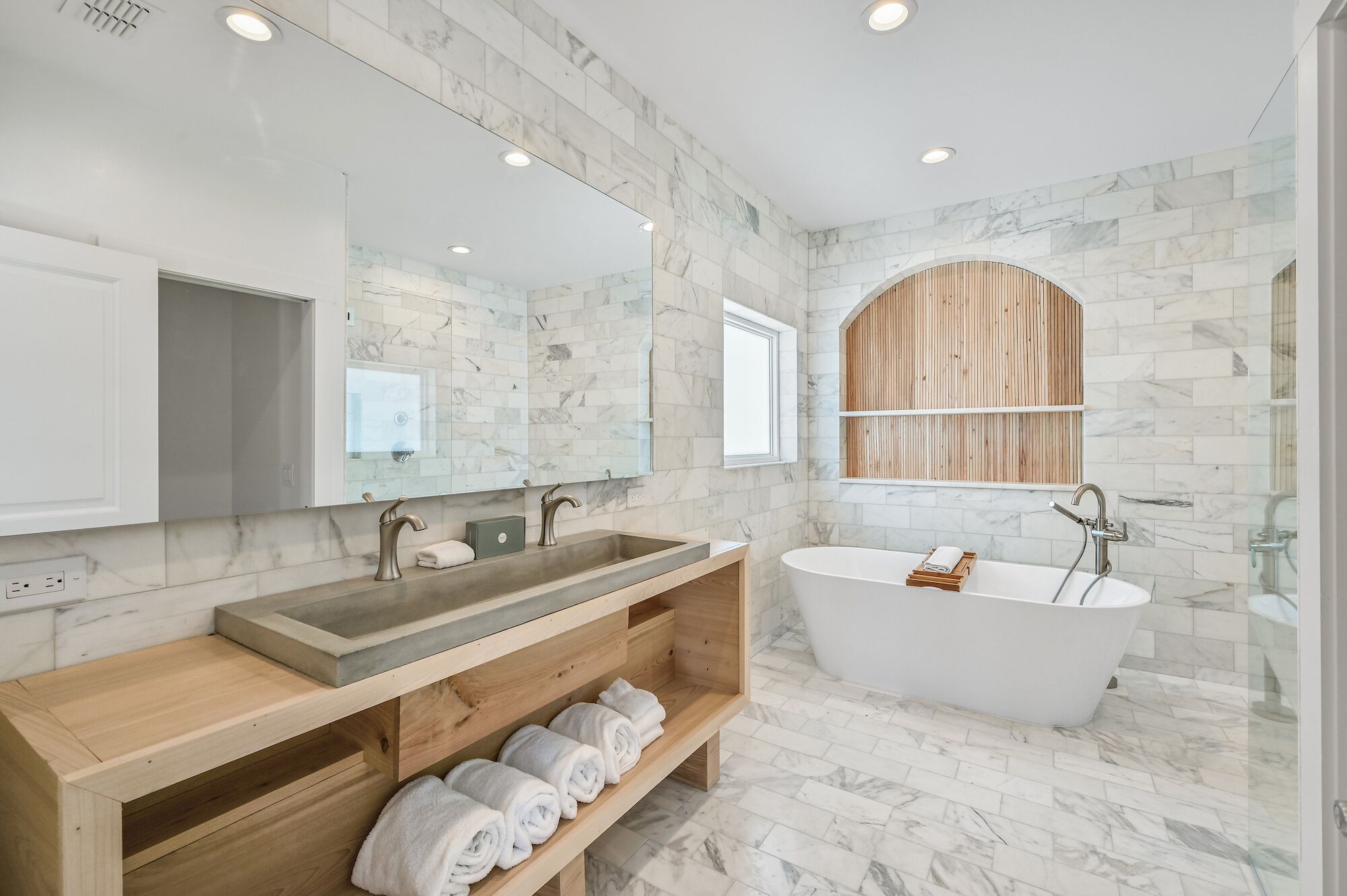 A modern bathroom with a freestanding bathtub, a double sink vanity, and a wooden shelf with towels.