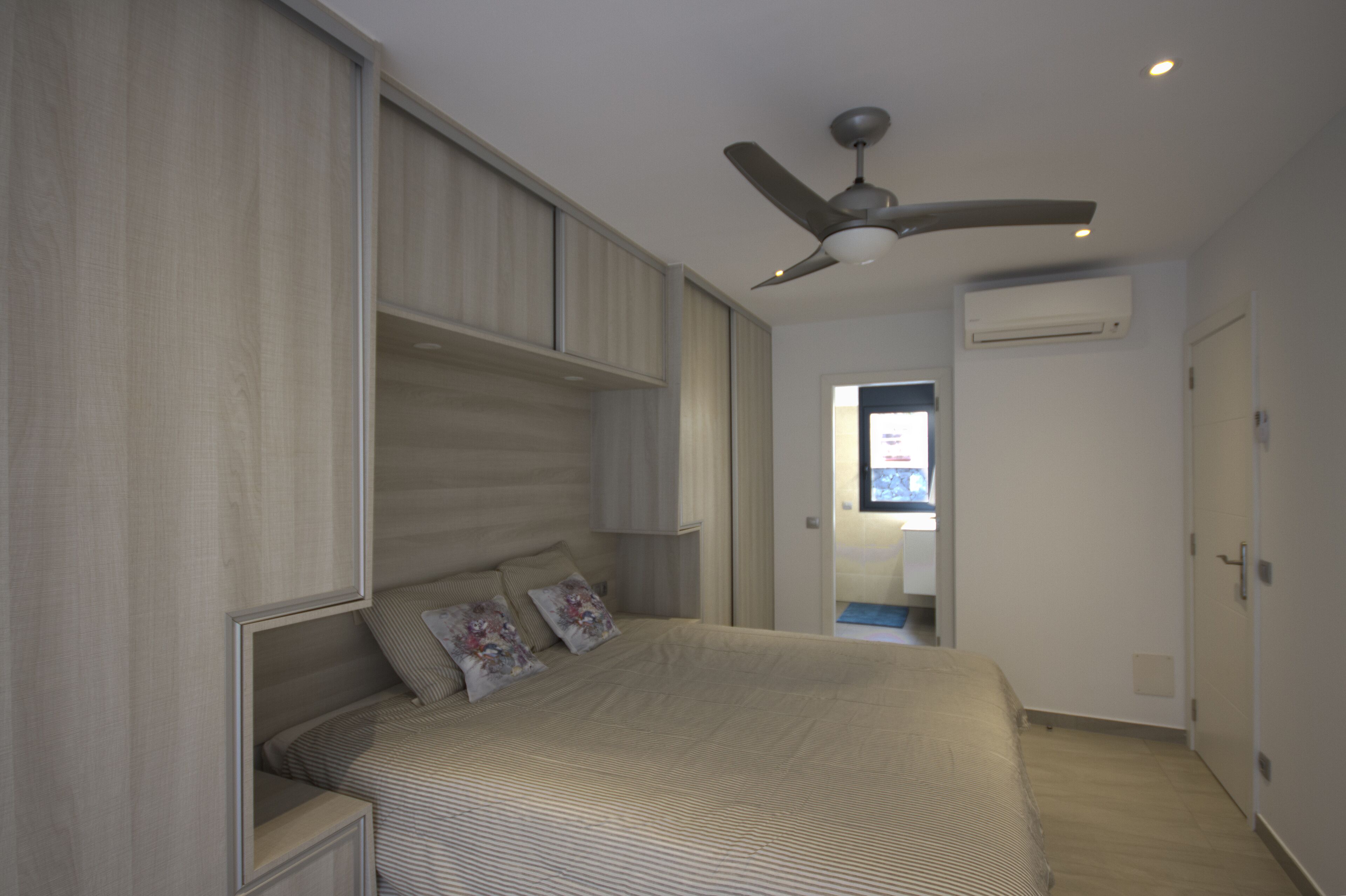 A bedroom with a bed, built-in shelving, a ceiling fan, and an air conditioning unit.
