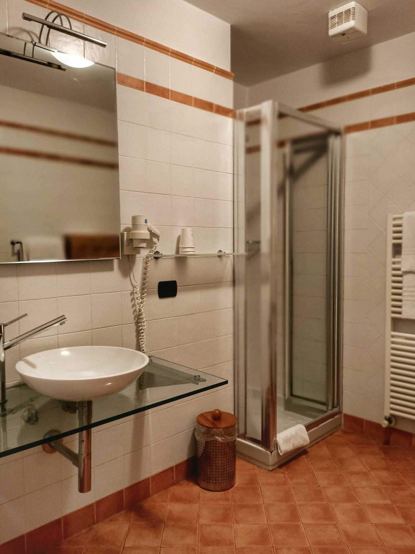 A bathroom with a glass sink, a mirror, a shower, and a towel rack.