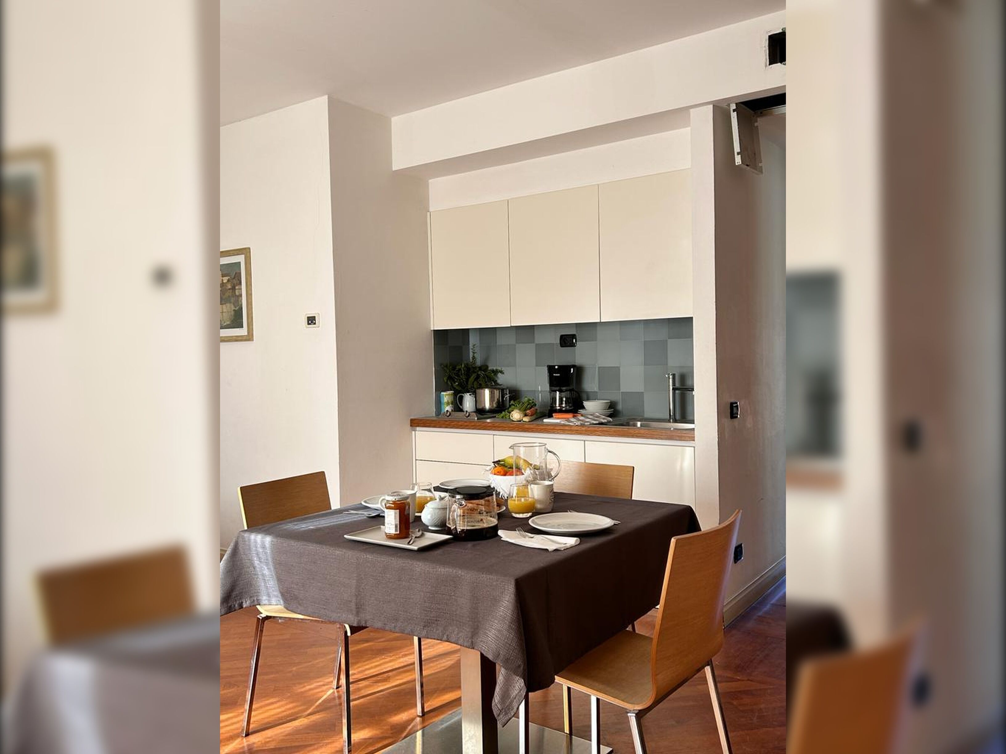 Un comedor moderno con una mesa lista para cuatro, una cocina al fondo y una puerta que da a otra habitación.