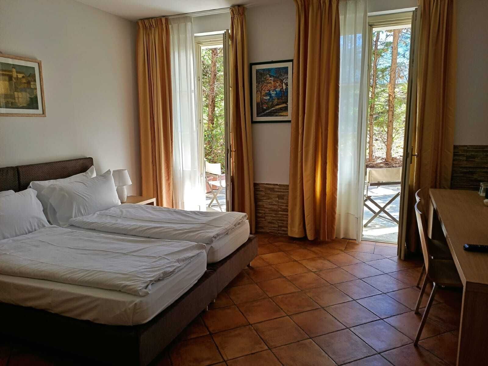 A hotel room with two beds, a desk, and a window with curtains.