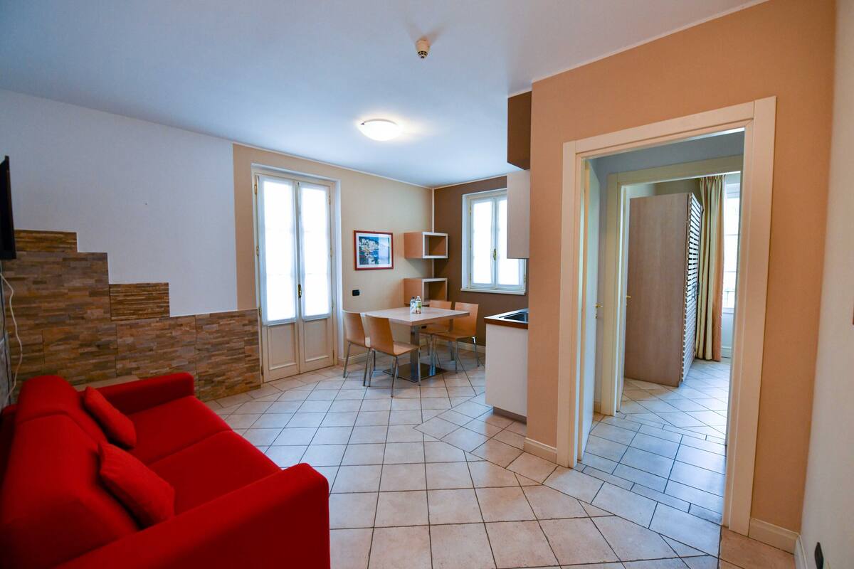 Een woonkamer met een rode bank, een eethoek met een tafel en stoelen, en een keuken.