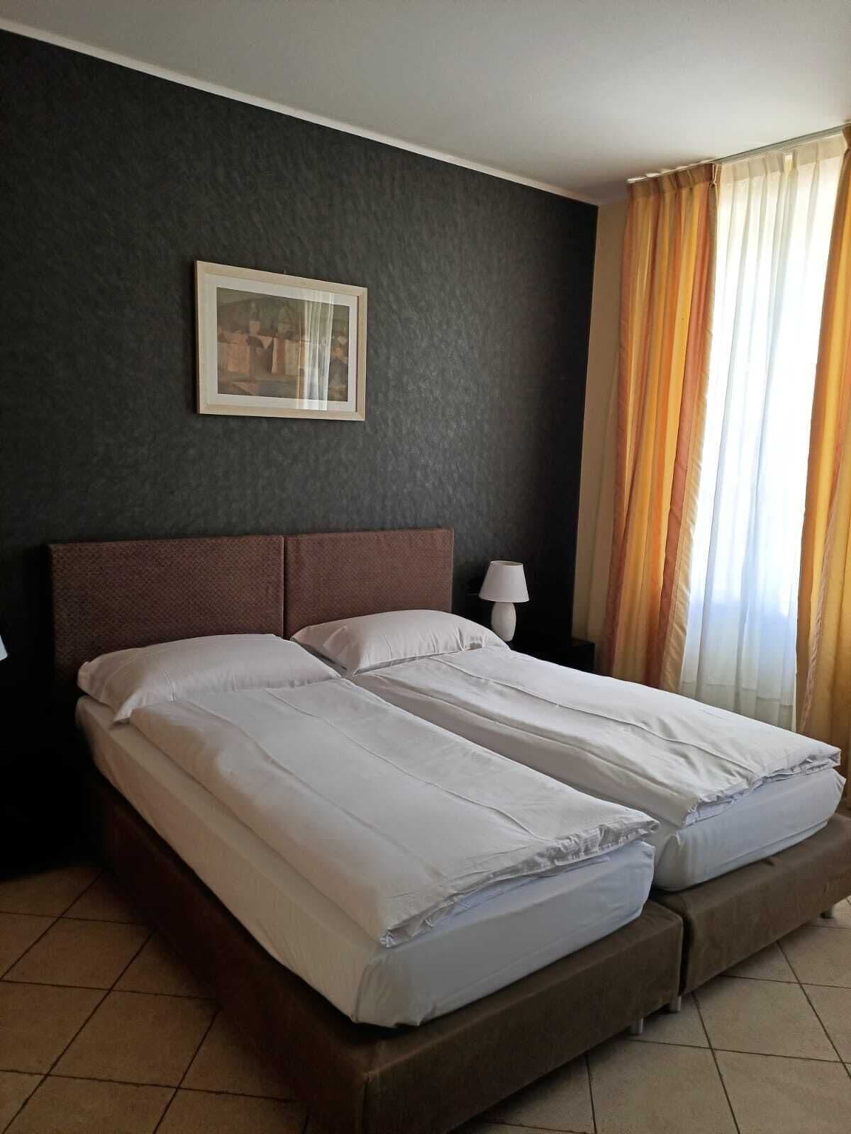 A double bed with white linens in a room with dark walls, a framed picture, and a window with curtains.