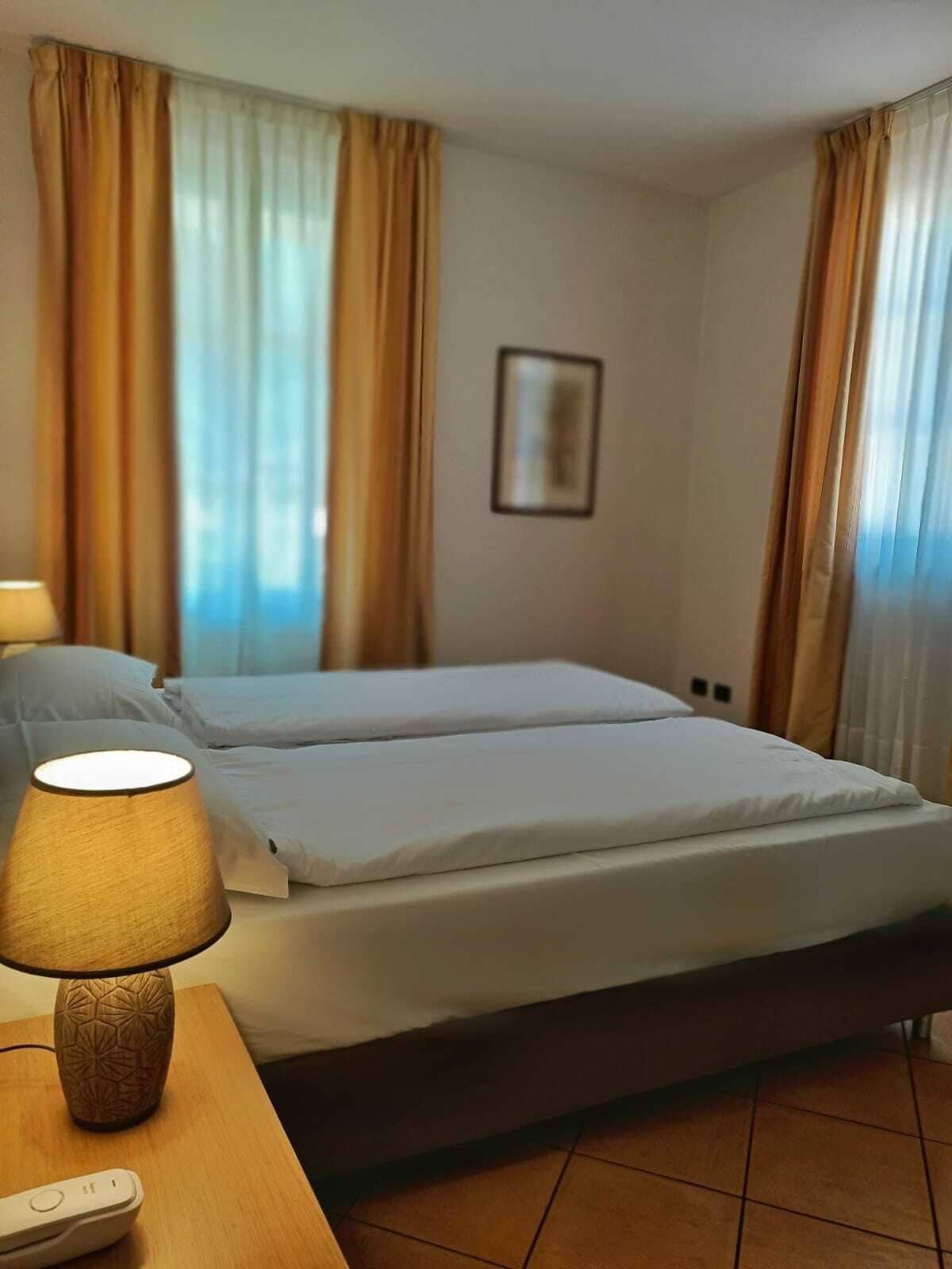 A hotel room with two beds, a lamp, a remote control, and curtains.