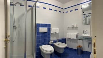 A bathroom with a glass shower enclosure, two toilets, a bidet, a sink, and a mirror.