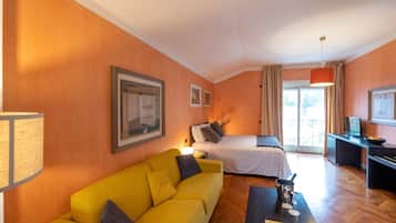 A hotel room with a yellow sofa, a bed, a desk, and a view of the outdoors.