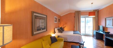 Habitación de hotel con sofá amarillo, cama, escritorio y vistas al exterior.