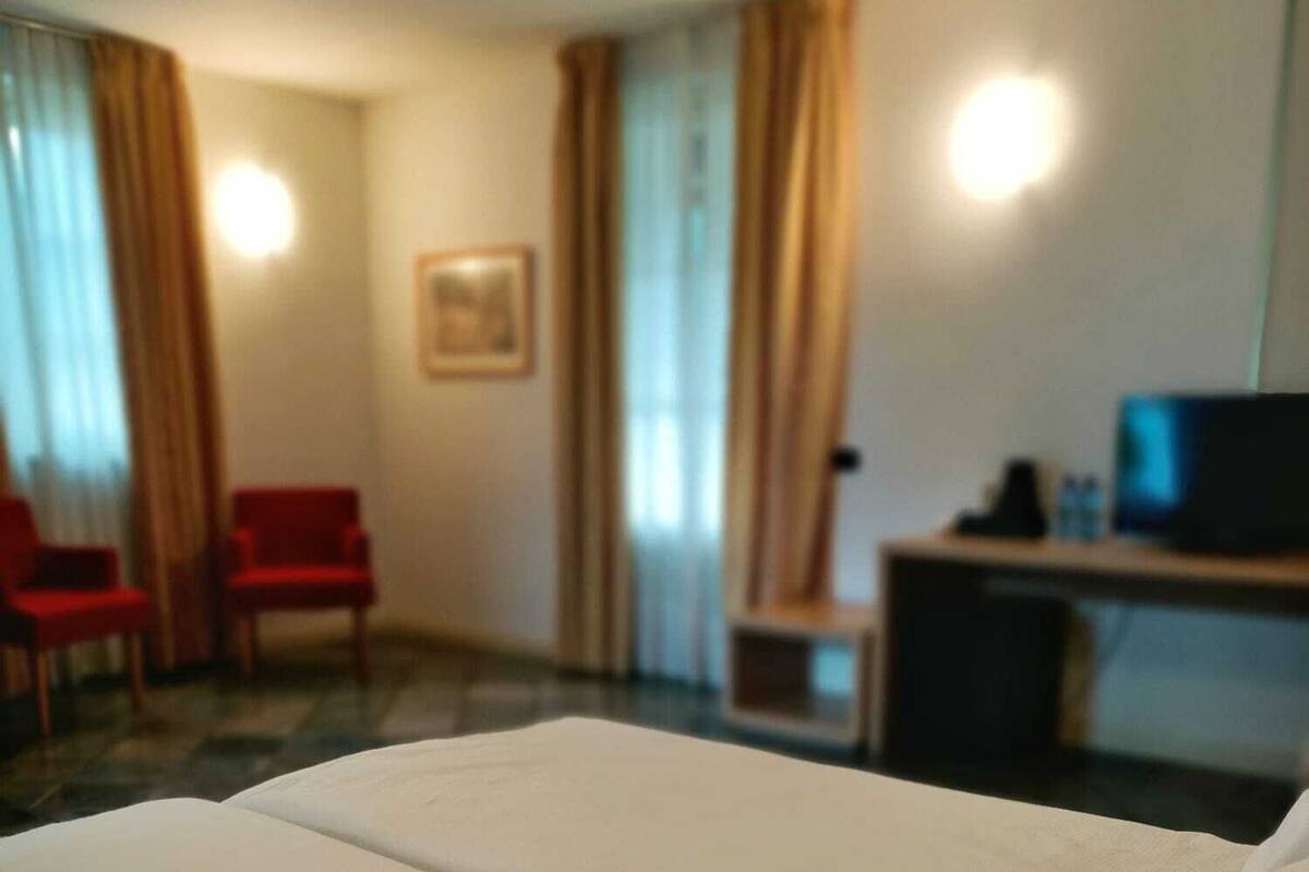 Een hotelkamer met een bed, een bureau met een computer en twee rode stoelen.