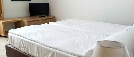 Habitación de hotel con una cama, una mesita de noche con lámpara, televisión y tres cuadros en la pared.