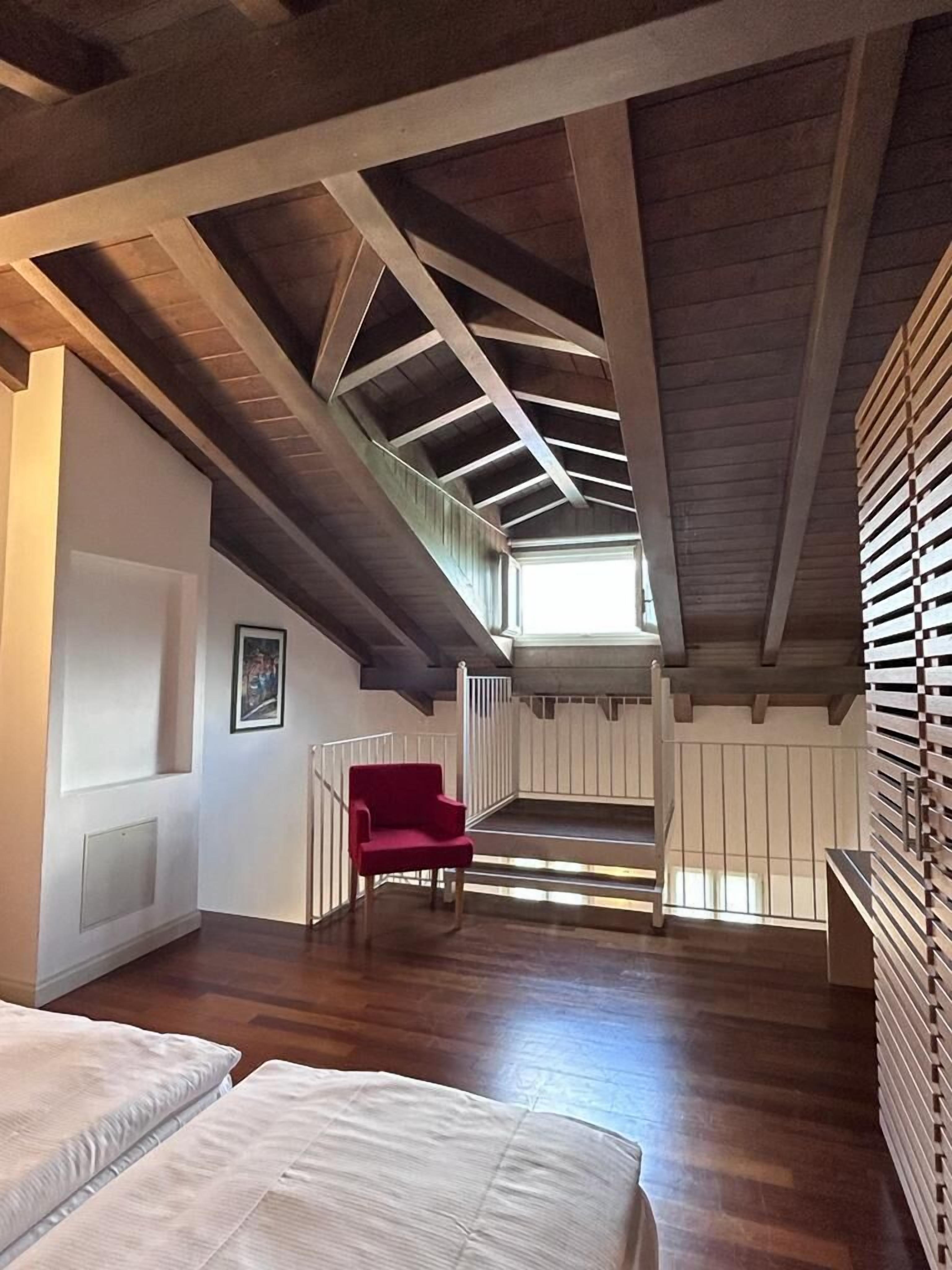 Una stanza con soffitto a falde, travi in legno, una sedia rossa e un letto.