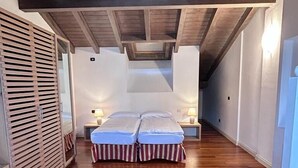 Une chambre avec un plafond en bois, un lit avec une literie à rayures, une chaise rouge et une table de chevet avec une lampe.