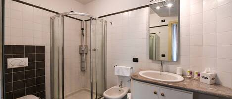 A modern bathroom with a glass-enclosed shower, a toilet, a bidet, and a sink with a vanity.