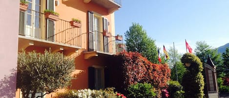 Un immeuble à plusieurs étages doté de balcons, un jardin avec différentes plantes et fleurs, et des drapeaux.
