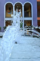 Uma fonte de água em frente a um edifício com varandas e plantas em vasos.