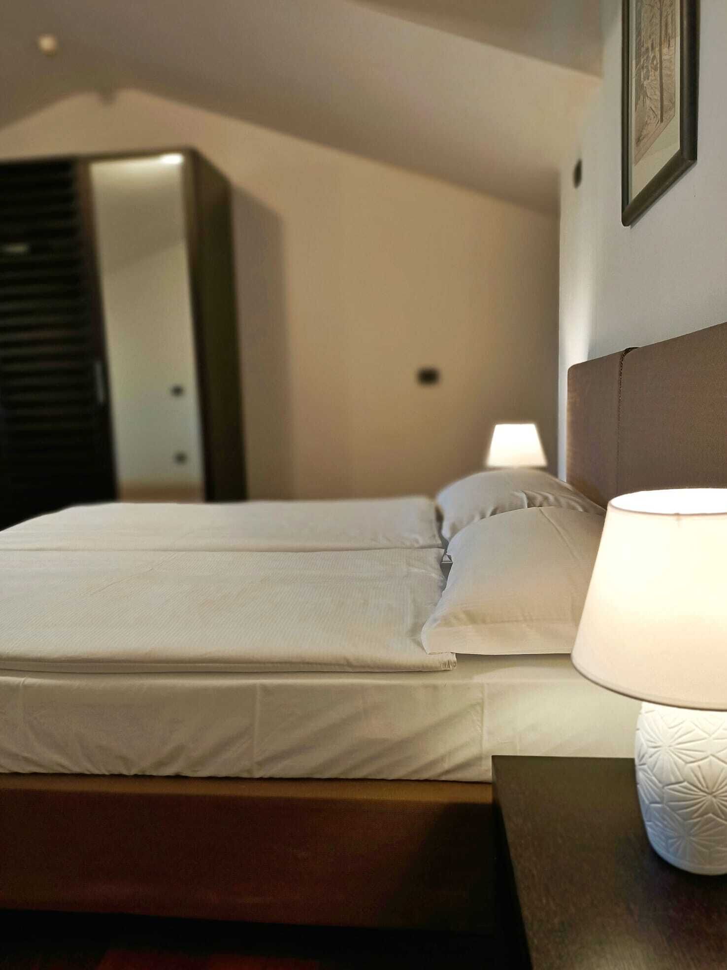 Una cama bien hecha con sábanas blancas, una lámpara de noche y un cuadro en la pared.