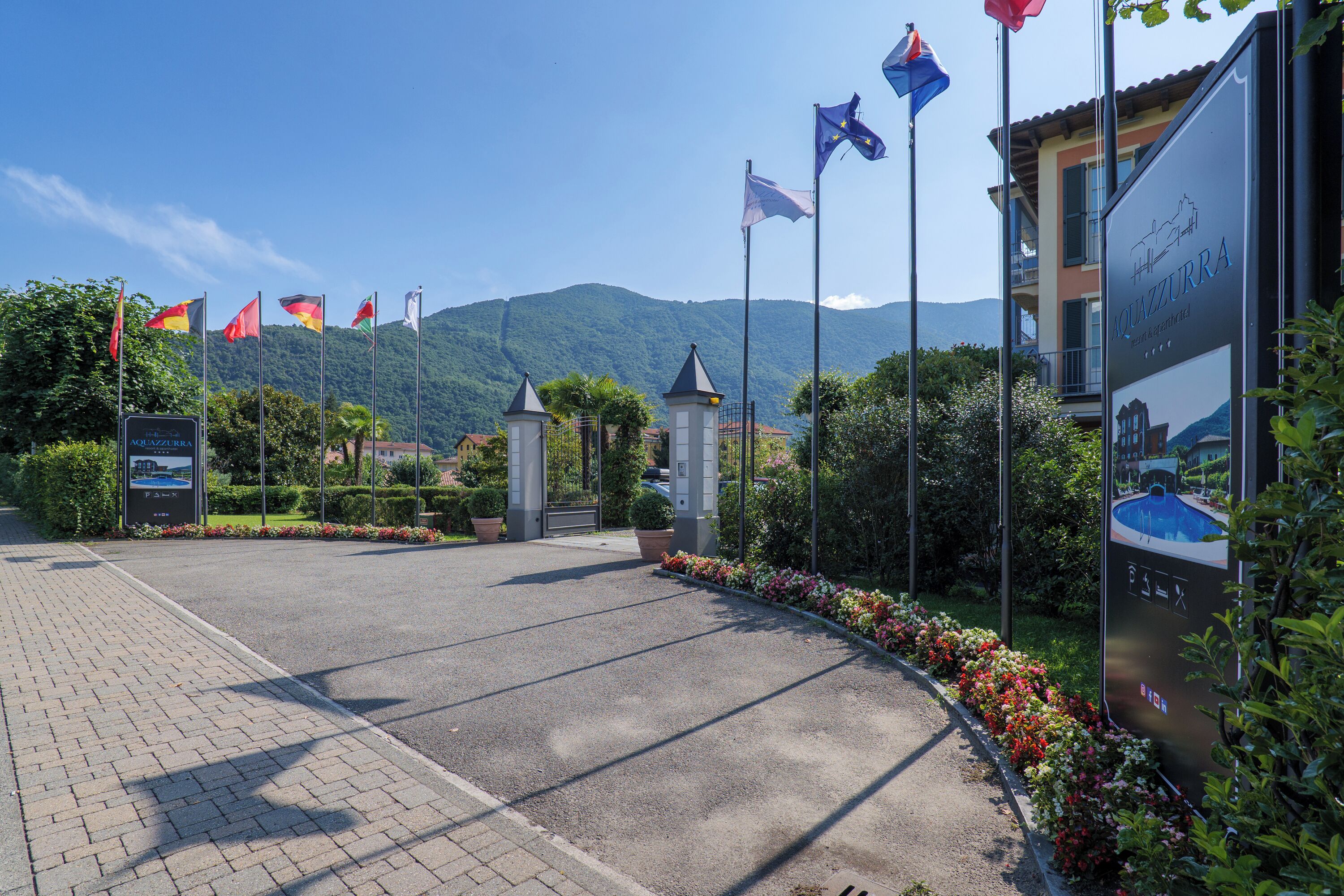 A hotel entrance with flags, a sign, and a mountainous backdrop.