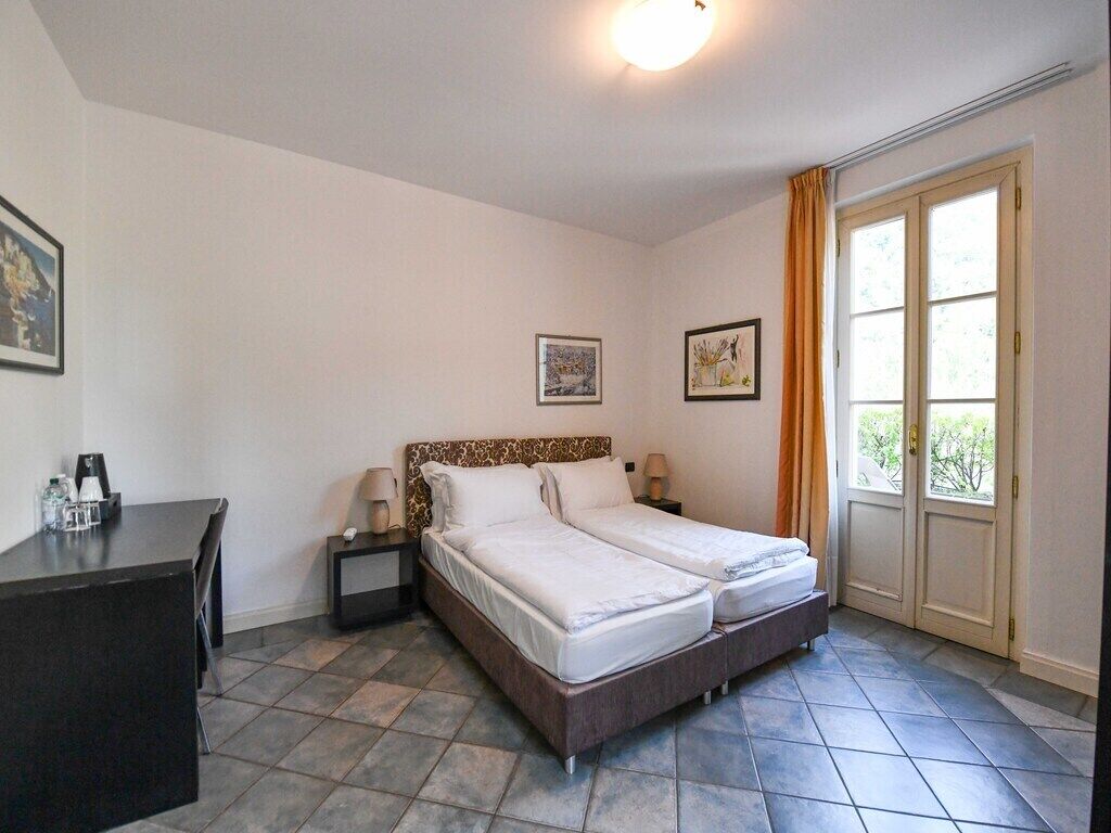 Un lit double avec une tête de lit à motifs, des tables de chevet avec des lampes, un bureau avec une chaise et une grande fenêtre avec des rideaux.