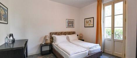 A double bed with a patterned headboard, bedside tables with lamps, a desk with a chair, and a large window with curtains.