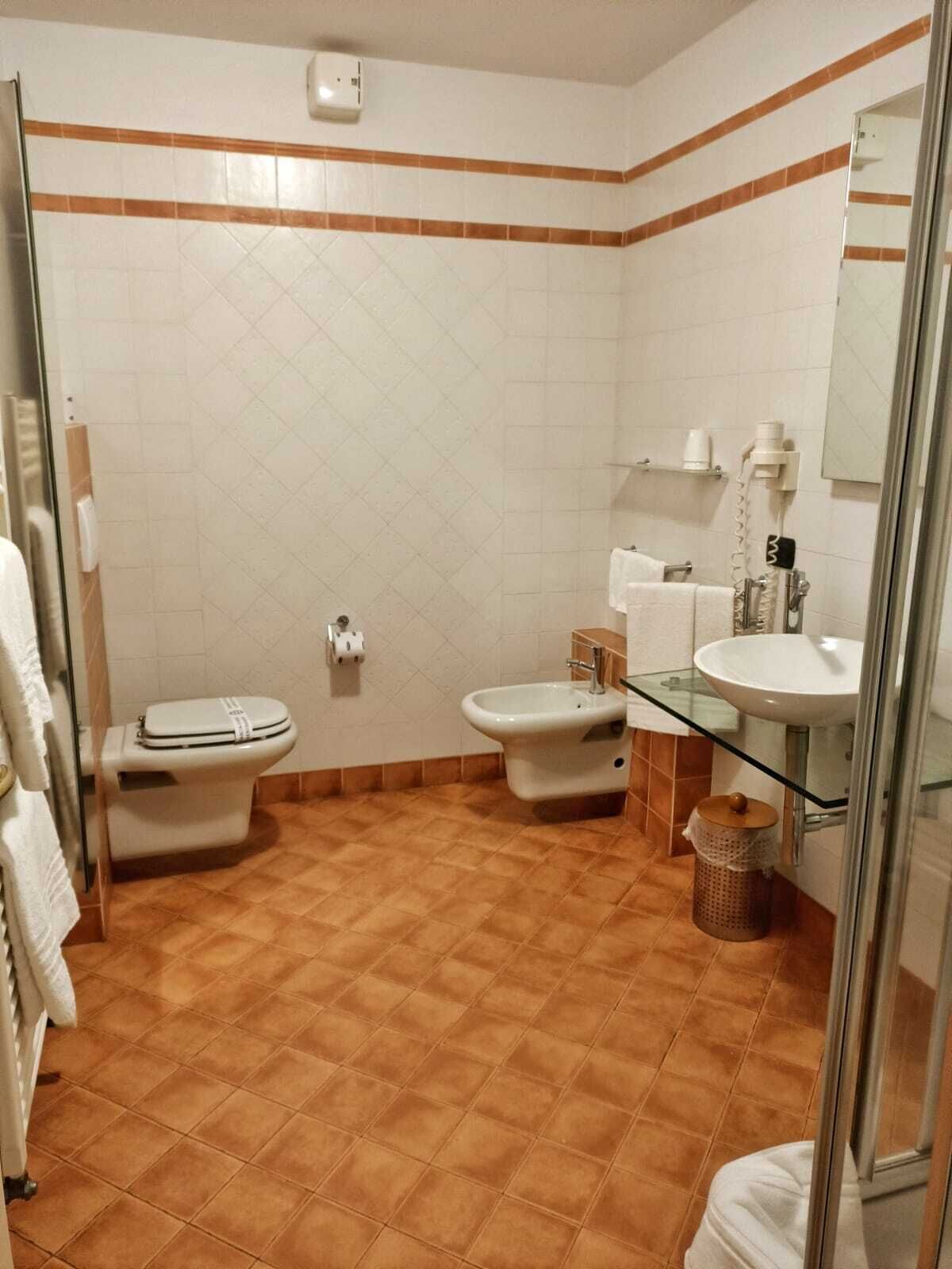 A bathroom with a toilet, bidet, and glass-enclosed sink.