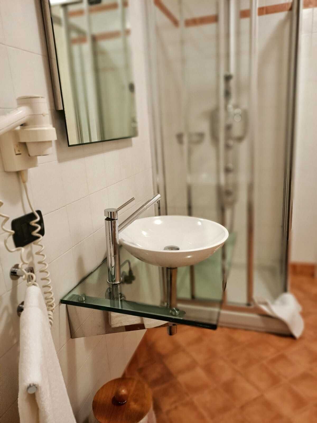 Ein Badezimmer mit einem Glaswaschtisch, einem Spiegel, einem Handtuchhalter und einer Duschkabine.
