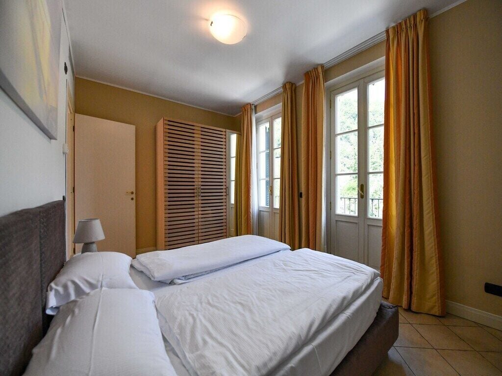A hotel room with a bed, a nightstand, a lamp, a window with curtains, and a door.