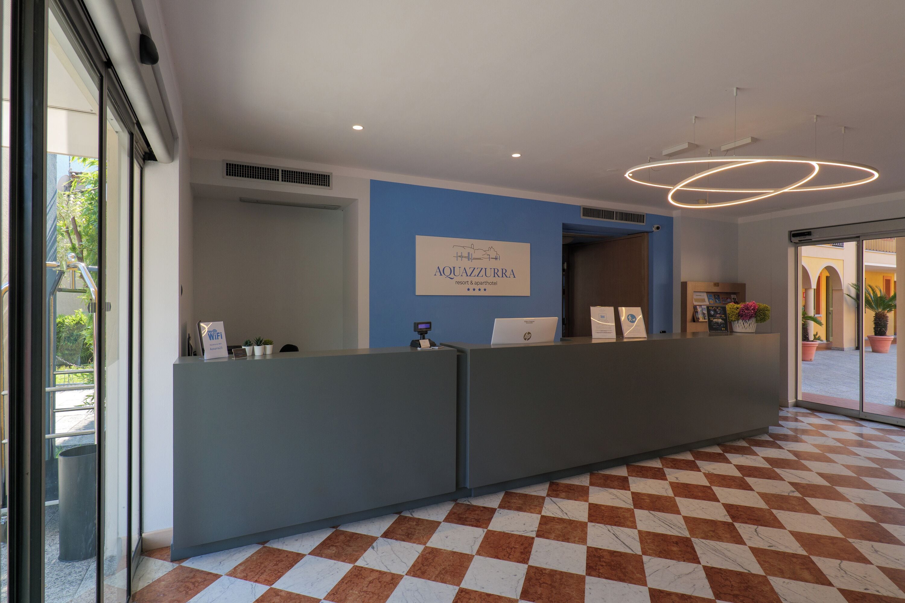 A reception area with a checkered floor, a reception desk, and a sign for Aquazzurra Resort & Spa.