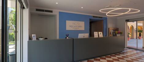 A reception area with a checkered floor, a reception desk, and a sign for Aquazzurra Resort & Spa.
