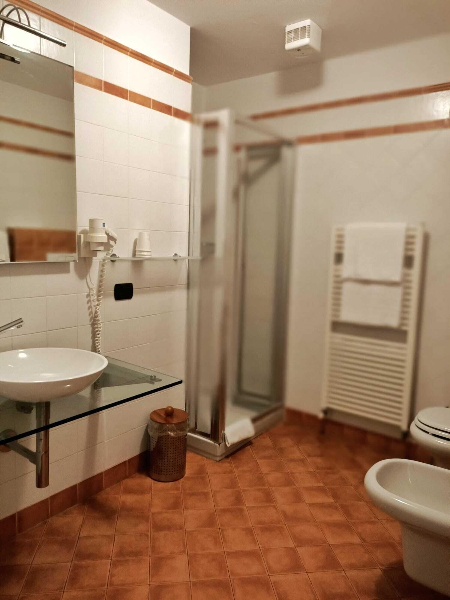 Een badkamer met een glazen wastafel, witte tegels, een douche en een toilet.