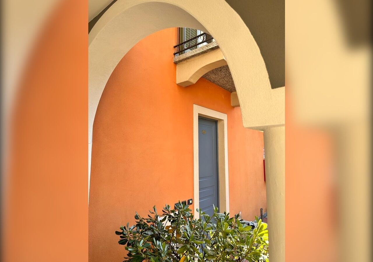 An orange building with a blue door, an archway, and some greenery in the foreground.