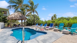A swimming pool with lounge chairs and a thatched-roof structure. - Reel Knotty ~ Pool Home, 35' Dock, Walk to the Beach, Bikes & Kayaks! (Marathon)
