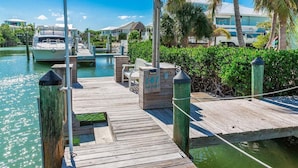A wooden dock with a boat, a small seating area, and a building in the background. - Reel Knotty ~ Pool Home, 35' Dock, Walk to the Beach, Bikes & Kayaks! (Marathon)