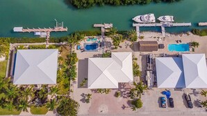 An aerial view of a resort with multiple buildings, a dock with boats, a swimming pool, and a small island with dense vegetation. - Reel Knotty ~ Pool Home, 35' Dock, Walk to the Beach, Bikes & Kayaks! (Marathon)