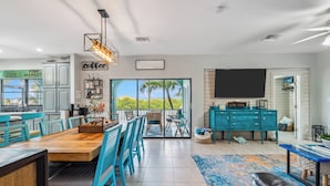 A modern kitchen with a large dining table, teal cabinetry, and a view through the glass door. - Reel Knotty ~ Pool Home, 35' Dock, Walk to the Beach, Bikes & Kayaks! (Marathon)