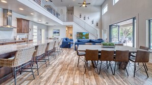A spacious kitchen with a high ceiling and a mezzanine level, a dining area with a large table and chairs, and a living area with a sofa and a TV. - Frio Ridge Retreat @ Frio Premier Rental Homes (Concan)
