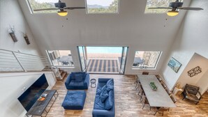 A spacious living area with a large sofa set, a dining table, and a view of the outdoor patio through large windows. - Frio Ridge Retreat @ Frio Premier Rental Homes (Concan)