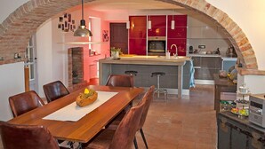 A modern kitchen with an arched brick ceiling, a central island, and a dining area with a wooden table and chairs. - Cascina IL SOGNO  (Cossano Belbo)