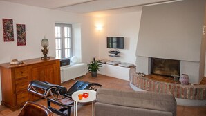 A living room with a fireplace, a sofa, a coffee table, and a TV mounted on the wall. - Cascina IL SOGNO  (Cossano Belbo)