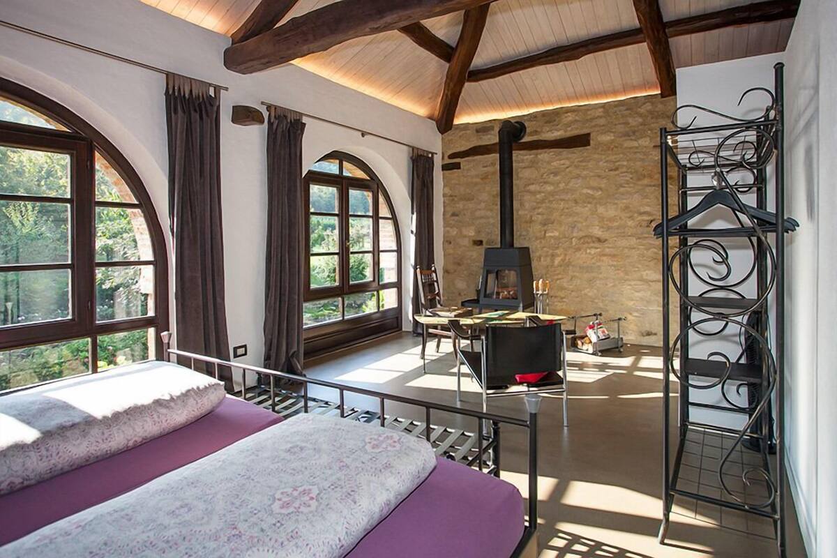 Quarto com cama, lareira e janelas amplas.