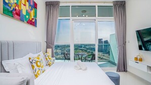 Una habitación de hotel moderna con una cama grande, un balcón con vistas a la ciudad y un televisor de pantalla plana en la pared.