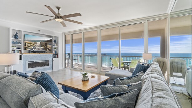 A spacious living room with a large sofa, a coffee table, and a television. There is a balcony with a view of the ocean. - Gulf Front 3/3 Resort w/Pool & 3 King Suites! Chair/umbrella set-up included! (Navarre)