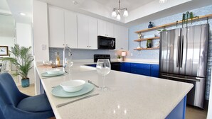 A modern kitchen with a central island, stainless steel appliances, and blue cabinetry. - Gulf Front 3/3 Resort w/Pool & 3 King Suites! Chair/umbrella set-up included! (Navarre)