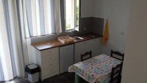 A small kitchen with a window, a sink, a table with a tablecloth, and a chair. - Eleonas apartment on the 1st floor with unobstructed ocean views (Rethymno)