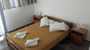 A neatly made bed with white pillows and folded towels, wooden nightstands with lamps, and a plain white wall. - Eleonas apartment on the 1st floor with unobstructed ocean views (Rethymno)