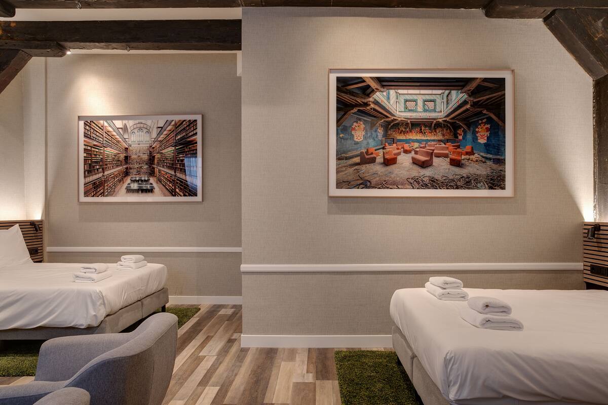 A hotel room with two beds, a large painting of a library, and a painting of an attic room.