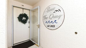 A white door with a black doormat, a number '206' above it, and a circular sign on the wall reading 'Seas The Quay est. 2023'. - Inlet View 2 BR Condo! Marlin Quay 206 (Garden City)