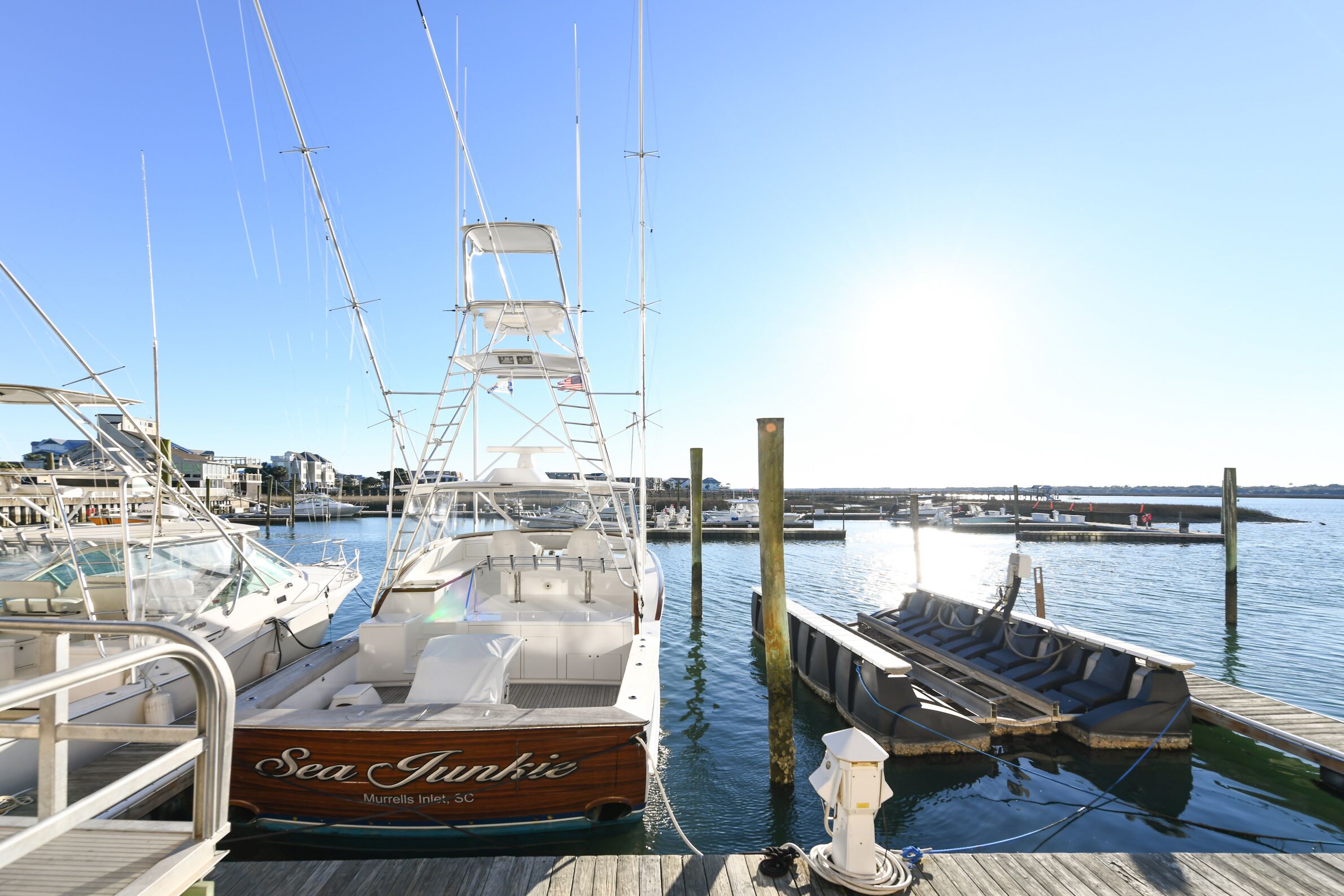 A marina with boats docked, a wooden dock, and a clear sky.