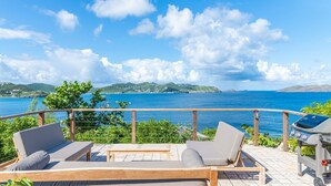 Eine Terrasse mit zwei Liegestühlen, einem Grill und einem schönen Blick auf das Meer und die Hügel.